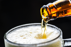 A bottle of beer being poured into a pint glass creating froth at the top of the glass