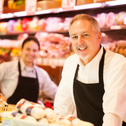 Two butchers looking into the camera from behind the counter