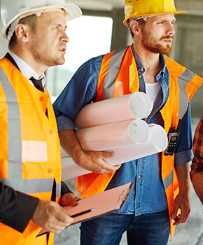 Two construction workers in safety vests and hard hats staring at their work