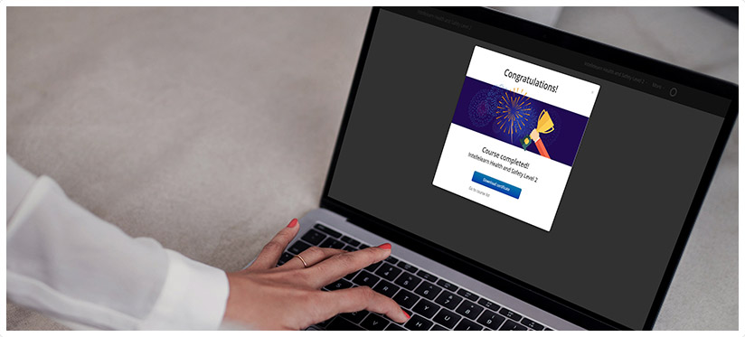 A hand on a laptop that has a congratulatory popup for completing an Intellelearn course